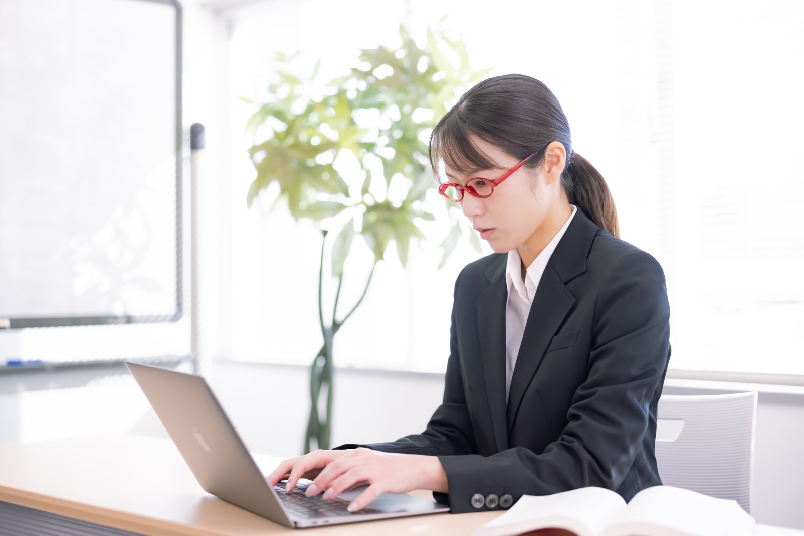 資料を参照しながら手元のPCで業務を進める女性