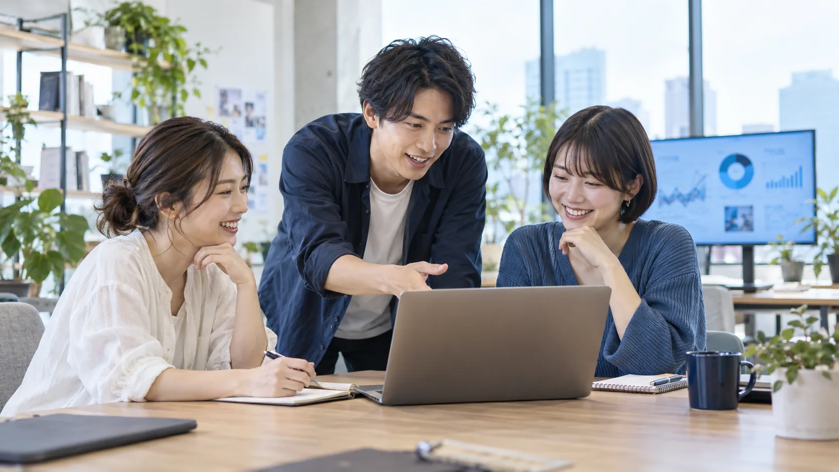 明るいスタジオでPCを囲み、アイデアを交わす若いチーム